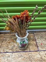 Full view of the hand-painted vase containing dried floral arrangement on wood floor with green background.