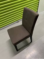 Full view of brown fabric modern chair with dark wooden legs on a light floor against a green wall