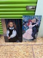 Two canvas art prints leaning against a green storage unit showing a young girl portrait and a dancing couple scene.