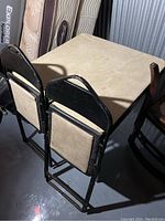 Photo showing folded chairs leaning against the card table, highlighting the beige upholstery and black metal frames.