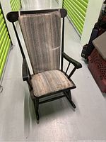 Front view of vintage wooden rocking chair with upholstered seat and back cushions in striped fabric, showing wear and moderate soiling.