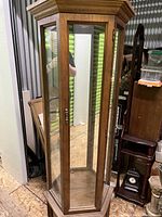 Full view of the wooden curio cabinet showing glass panels, wood framing, and mirrored interior visible through glass.