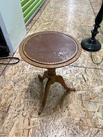 Image of round wooden plant stand with leather top, tripod base, visible minor wear on leather surface.