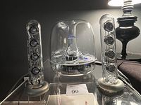 Front view of two transparent satellite speakers flanking transparent dome subwoofer on reflective surface