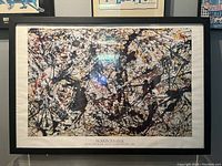 Framed Jackson Pollock print displayed on wall with abstract splattered paint in multiple colors.