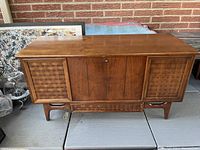 Front view of a mid-century wooden storage chest with two woven wood panel doors and center door with lock.