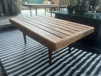 Three-quarter view of bench showing slatted top and tapered legs