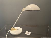 Full view of the vintage Jen Yang Atomic table lamp with white rounded base, angled arm, and dome shade on clear surface.
