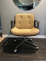 Front view of chair showing beige button-tufted upholstery, black shell arms, chrome caster base