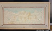 Frontal view of the framed hand cast paper artwork depicting a Pueblo building with textured paper elements and pastel colors, set in a wooden frame.