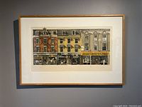 Framed lithograph depicting urban street storefronts.