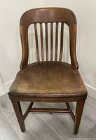 Front view of a wooden chair with a curved backrest and vertical slats, showing seat and legs.