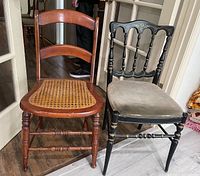 Photo of two wooden chairs side by side; one with cane seat and natural wood finish, the other painted black with upholstered seat and decorative backrest