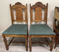 Pair of wooden chairs with ornate carved backs and blue-green fabric seats placed on a light-colored floor with a woven basket visible in the background.