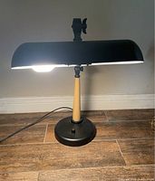Desk lamp turned on showing black metal shade, wooden support, and black base with on/off switch