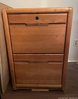 Image of a wooden two-drawer filing cabinet with integrated recessed horizontal handles and lock on top drawer. Light oak finish and rounded edges on front frame.