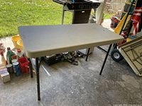 Light gray folding table with black legs located indoors in a garage or storage area.