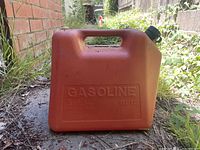 Red plastic 5-gallon gasoline container shown outdoors on the ground with visible embossed branding and capacity markings on front.