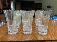 Six glasses are grouped showing the ribbed vertical design and thick wall thickness of the glass on a wooden table.