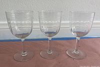 Photo showing three matching clear glass wine glasses with textured patterns near the top of the bowls, short stems, and flat bases.