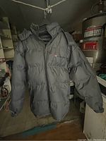 Black men's puffer jacket hanging indoors, showing front and long sleeves.