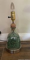 Green Patron bottle made table lamp with brass socket and clear flame-shaped bulb, on/off knob switch, mounted on a metallic base, no lamp shade.