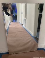 Large rectangular mirror standing against wall reflecting a hallway, showing the chip on the bottom right corner.