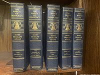 Five hardcover volumes of 'The March of Democracy' by James Truslow Adams, arranged side by side on a wooden shelf, showing spines clearly.