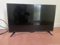 Photo of a black 32-inch Insignia LED TV placed on a flat surface, powered by an attached cord. The screen is off and reflective.