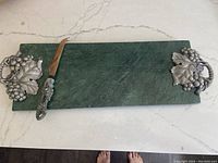 Green stone cheese plate with metal grapevine handles and cheese knife with matching grape handle placed on stone plate