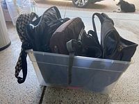 Clear plastic bin filled with multiple backpacks and fanny packs in various colors and styles.