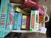 Photo showing a bin containing multiple board and card games including Risk, Scrabble, Monopoly Jr., Sorry, The Game of Life, The Chameleon, What Do You Meme, and Uno games.