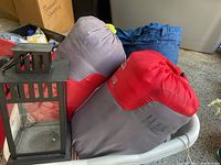 Three sleeping bags packed in sacks (red/gray, gray, blue) and black lantern sitting on a surface