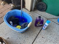 Photo showing a blue plastic bucket with metal handle containing several cleaning cloths. Next to the bucket are a purple bottle of 303 Car Wash shampoo and a white and blue can of Armor All Car Wash spray.