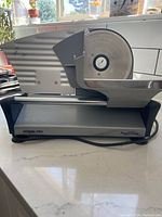 Side profile view of Waring Pro Food Slicer showing blade, slider tray and base with power cord coiled