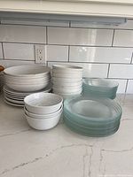 Multiple stacks of ceramic bowls and plates alongside stacks of glass plates on a kitchen counter.