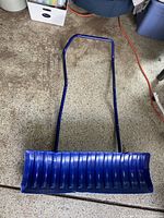 Image showing a large blue snow shovel with a wide plastic blade and a blue metal handle designed for snow removal.