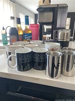 Ninja coffee machine on kitchen counter with four bottles of coffee syrups, multiple coffee mugs including Star Wars design and stainless steel tumblers in front.