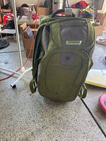 Front view of the green rolling luggage bag showing multiple zippered compartments and telescoping handle.