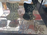 Six West Elm dining chairs with metal legs and wooden backs and seats, two chairs with black floral design, four with wood grain finish