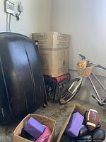 Black Subaru roof cargo box leaning against wall among other household items in a garage or storage area.