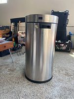 Large round stainless steel trash can with removable push lid showing wear and scuff marks.