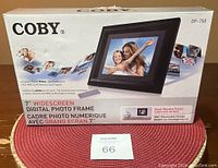Front of the box showing Coby 7" widescreen digital photo frame, model DP-758, with features such as no PC required, SD/MMC/MS memory card support, and wall-mountable design.