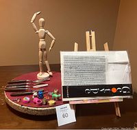 Full lot displayed on a surface with wooden human figure sketching model, palette cutters, erasers, easel, and rub-down lettering visible
