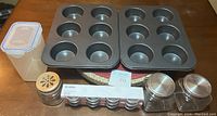 Overview of two metal baking trays for 12 muffins each, three glass jars, three packages of IKEA Blanda mini glass bowls, and one plastic storage container with locking lid.