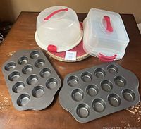 Two metal muffin/cupcake tins and two plastic carriers with red handles. One tin holds 15 muffins/cupcakes, the other holds 12. One carrier is round dome-shaped, the other is rectangular with a flat-top lid.