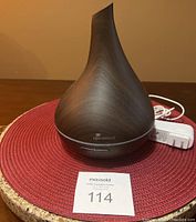 Photo of Diffuserlove essential oil diffuser with visible power adapter on a red placemat, shown from front angle.