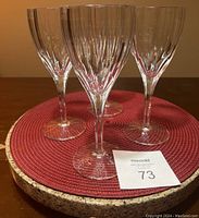 Four crystal wine glasses standing upright on a round cork and red placemat, showing vertical cut detailing on the bowl and clear stems.