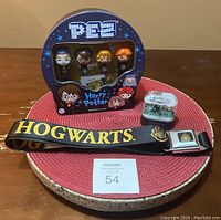 Four Harry Potter PEZ dispensers still in original tin packaging, small Harry Potter snow globe, and black Hogwarts belt with crest and text displayed on round placemat.