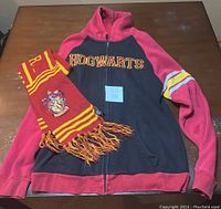 Photo showing the oversized Harry Potter Hogwarts hoodie laid flat with the Gryffindor scarf folded and placed on top at the left side, both items on a wooden table.